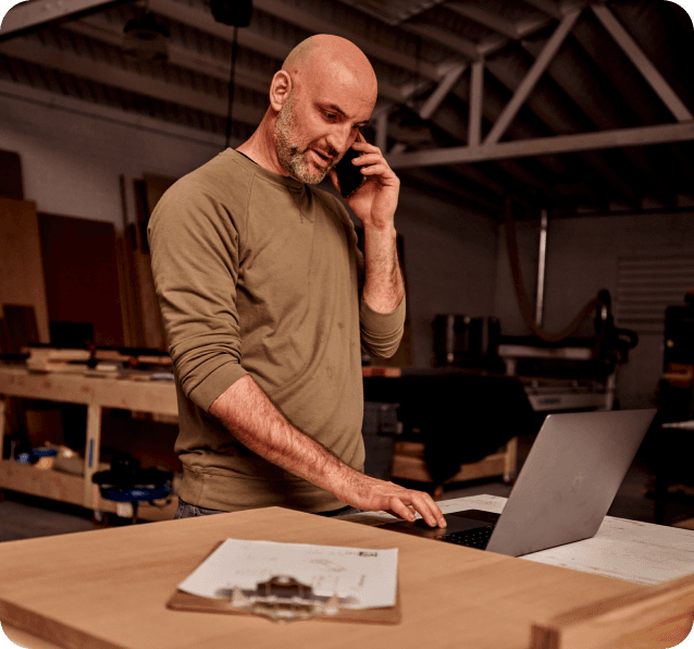 A worker chatting on the phone while looking at a laptop